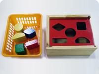 5 pièces en bois colorées posées dans un panier, à côté une boîte ajourée de différentes formes
